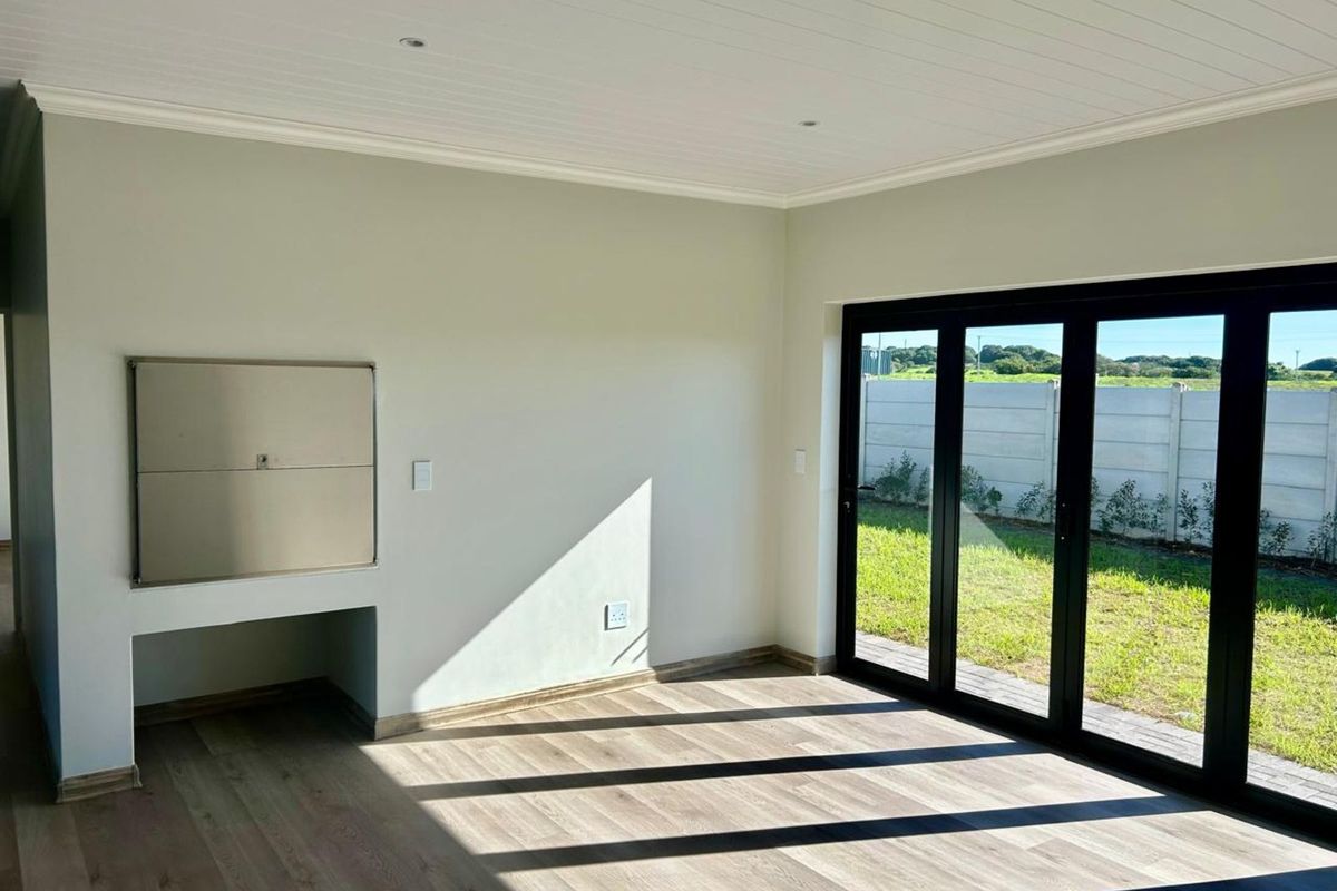 A bright living area featuring wood-look flooring, a built-in stainless steel braai, and large black-framed folding doors opening to the garden.