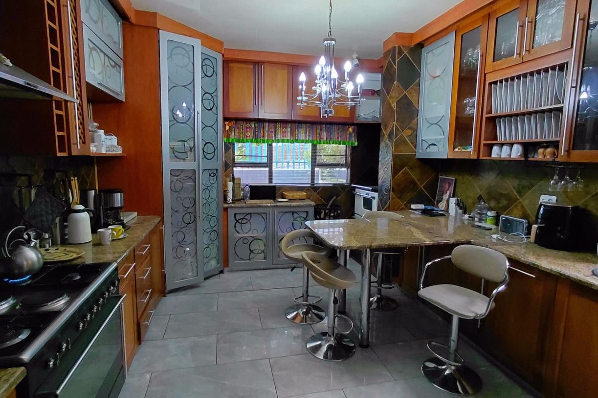 A traditional kitchen featuring wood-toned cabinetry, granite countertops, a built-in gas stove, and a central breakfast bar area with tiled flooring.