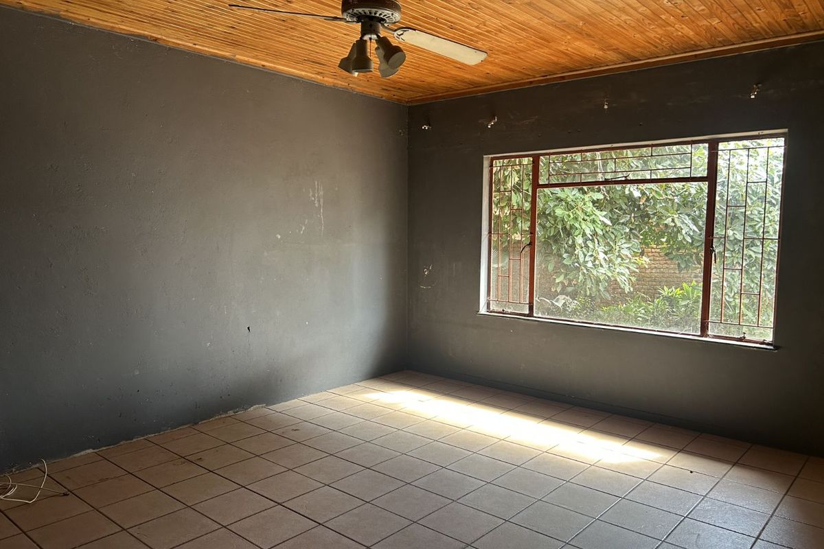 An empty living room featuring dark painted walls, tiled flooring, a wooden tongue-and-groove ceiling, and a ceiling fan.