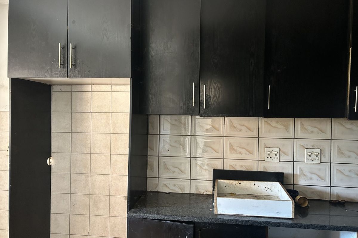 A dated kitchen area featuring dark wood-look cabinetry, granite countertops, and tiled splashbacks, currently requiring maintenance and cosmetic updates.