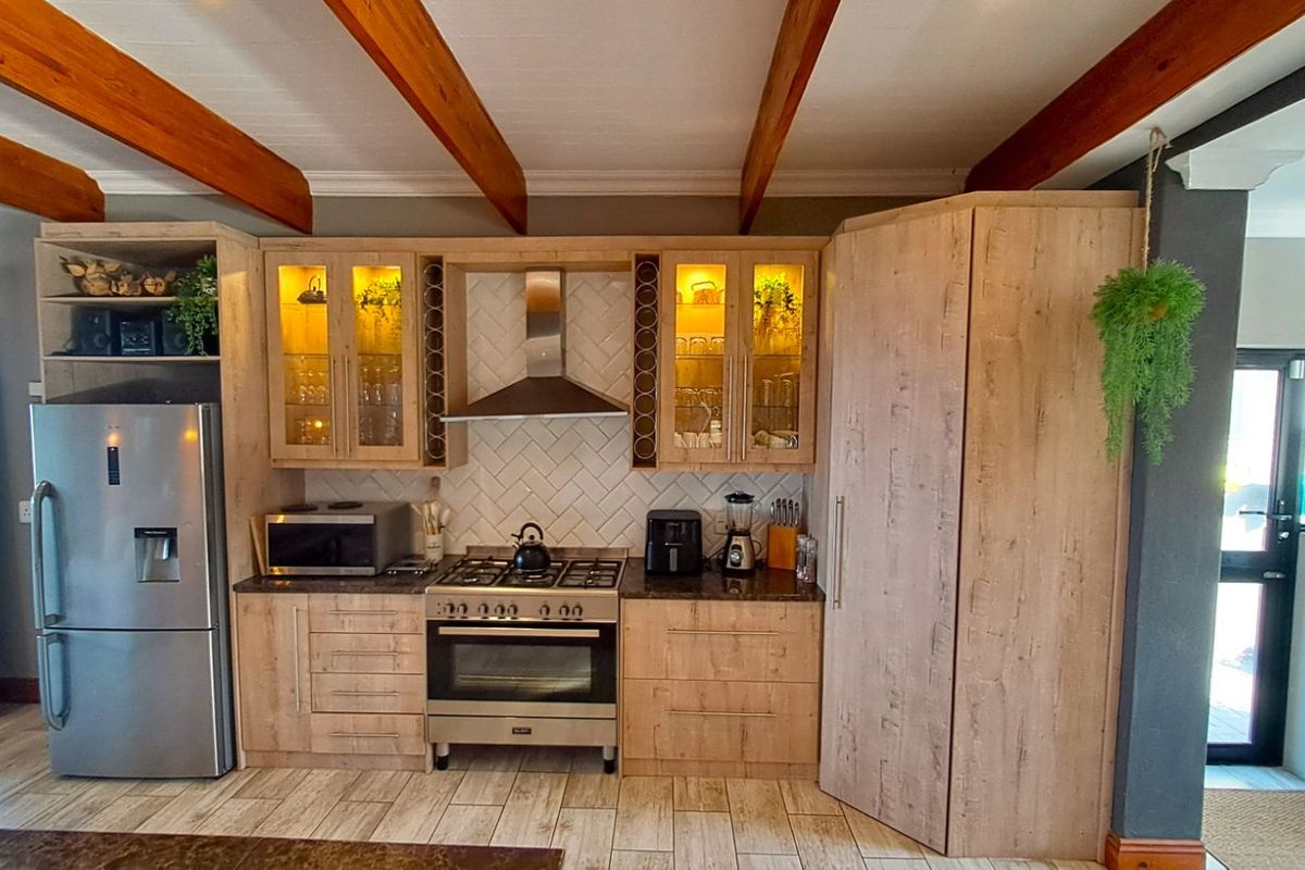 Modern kitchen featuring light wood cabinetry, herringbone tile backsplash, stainless steel gas stove with extractor fan, and exposed timber ceiling beams.