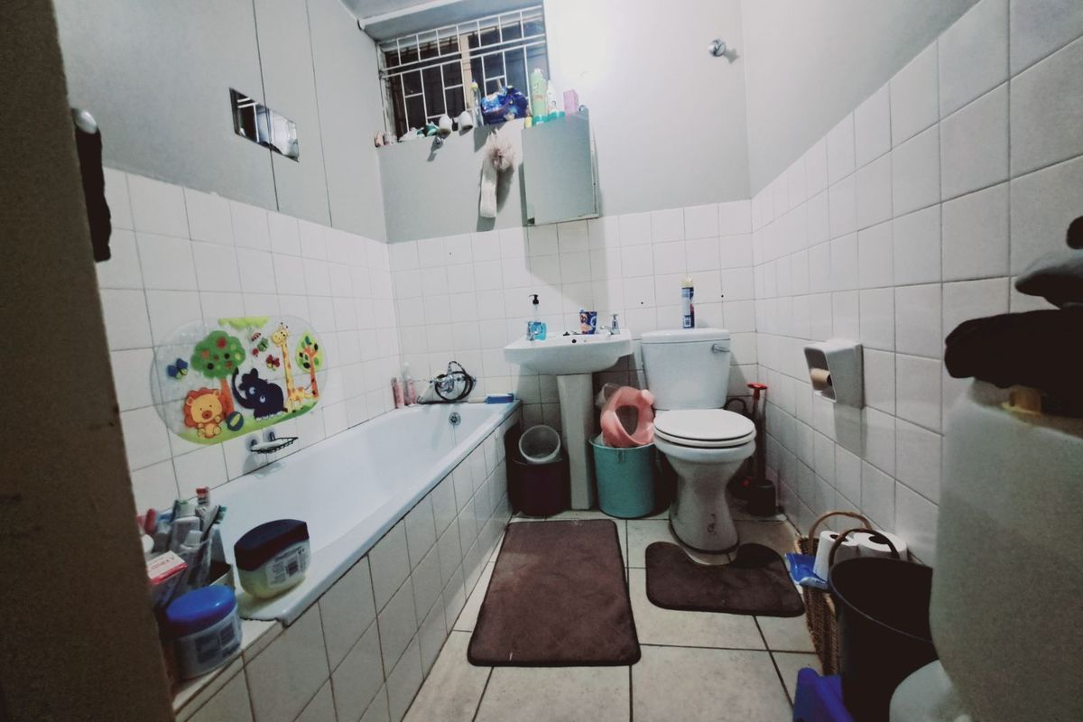 A functional bathroom featuring a standard bathtub, pedestal basin, and toilet with white wall tiling and tiled flooring.