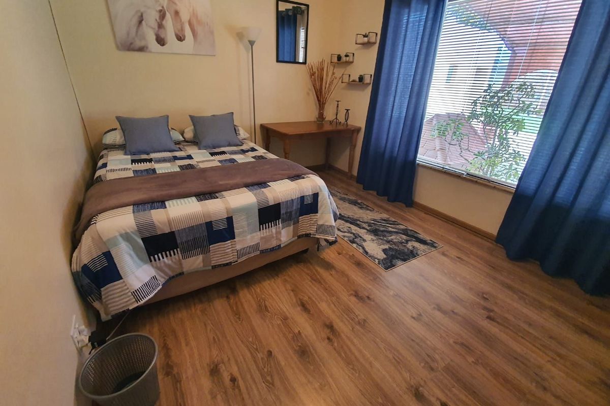 A well-lit bedroom featuring wood-look laminate flooring and a large window with blinds, providing a comfortable and functional living space.
