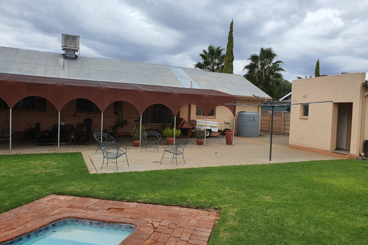 Rear exterior view featuring a paved patio area with a shade structure, a swimming pool, and a well-maintained lawn.