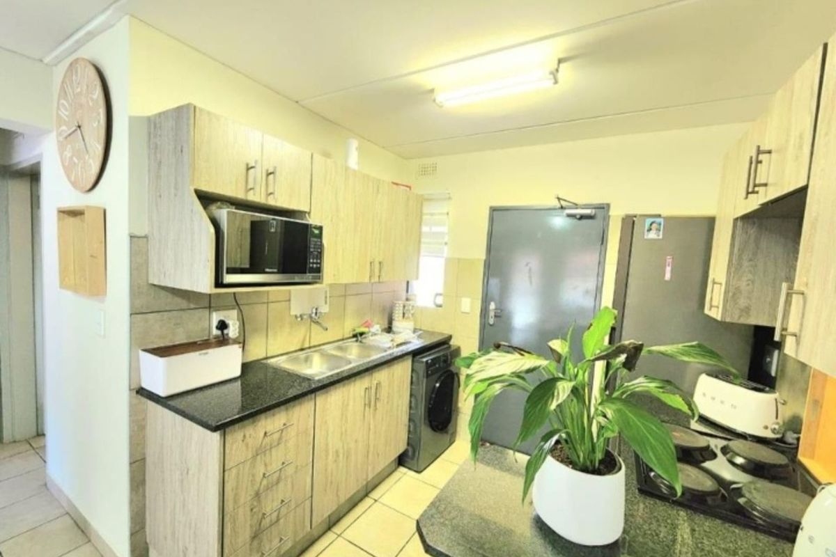 Compact kitchen featuring light wood-grain cabinetry, dark granite countertops, a double sink, and integrated space for a washing machine.