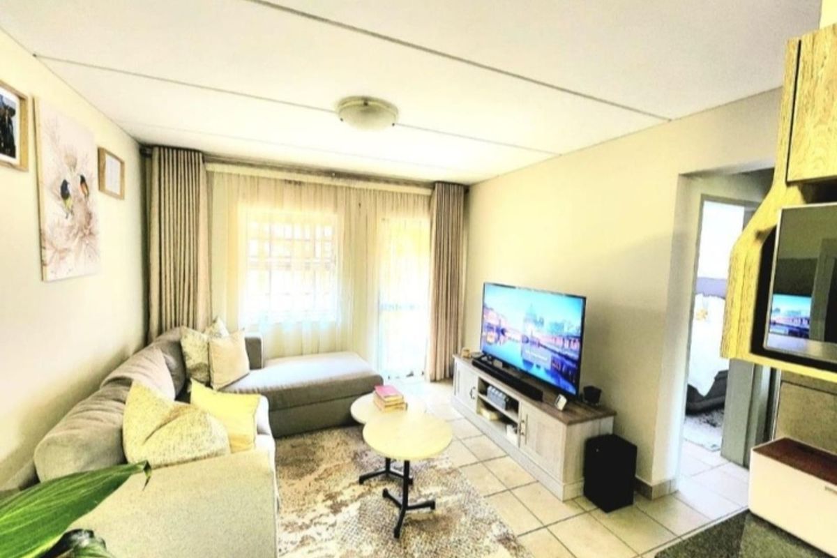A bright living room featuring tiled flooring, large windows with curtains, and a seamless transition to the adjacent living space.