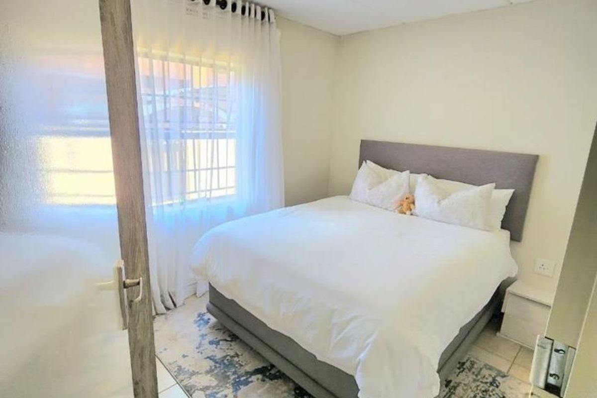 A compact bedroom featuring tiled flooring, a neutral color palette, and a window with sheer curtains, providing a functional and comfortable sleeping space.