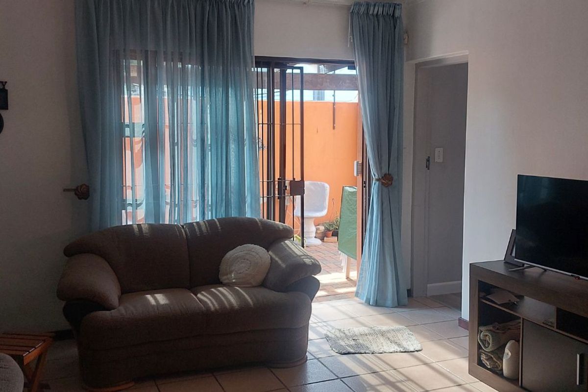 A living room featuring tiled flooring and a sliding glass door with security gate leading to an outdoor patio area.