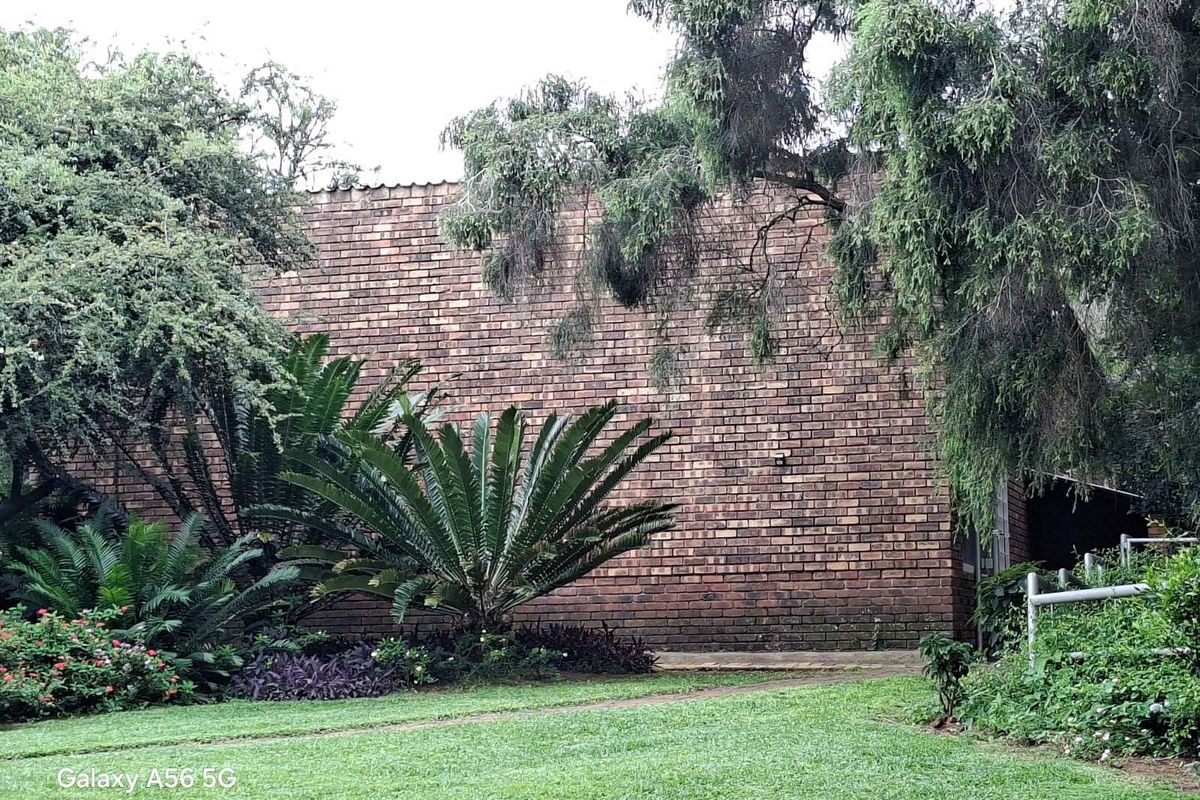 A view of the rear exterior brick facade of the house, featuring a landscaped garden with mature trees and established shrubs.