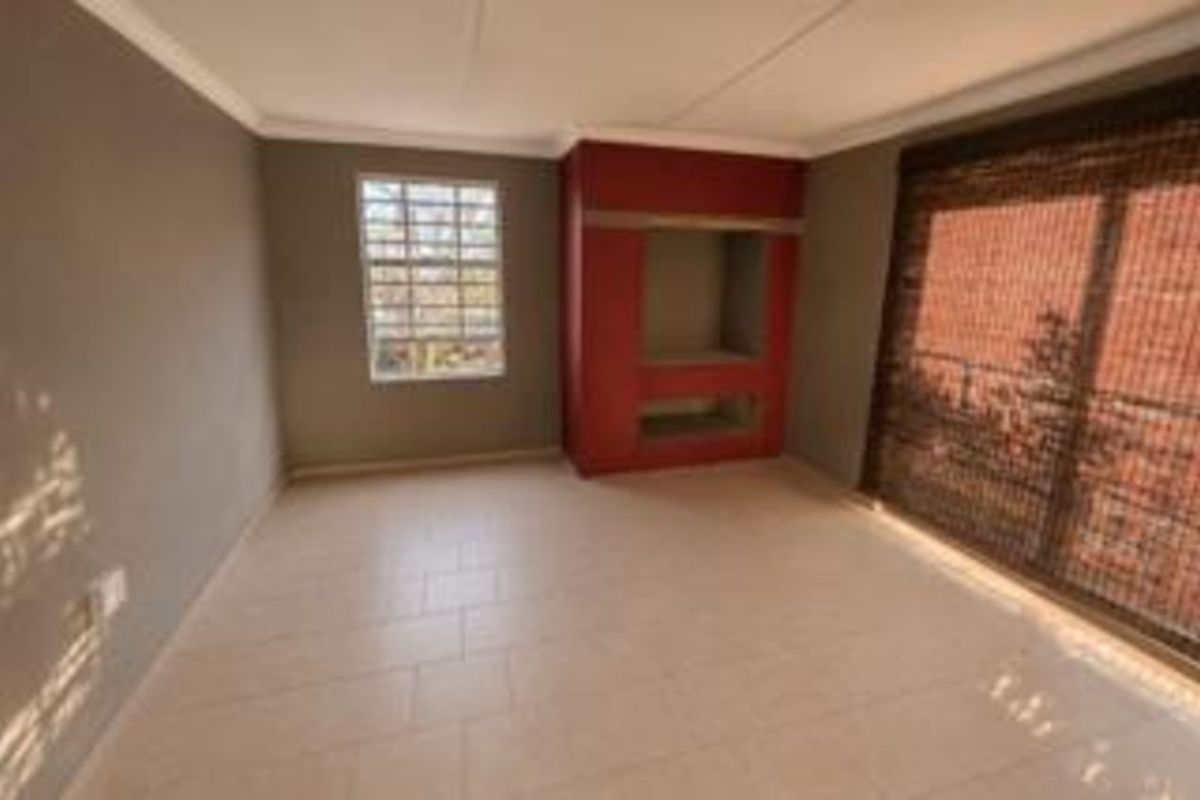 A bright living room featuring tiled flooring, a built-in media unit, and large windows with blinds, offering a clean and functional living space.