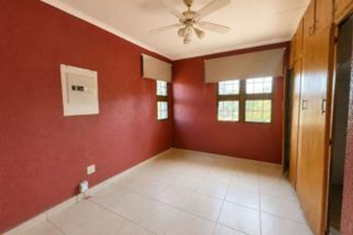 A bedroom featuring tiled flooring, built-in wooden cupboards, a ceiling fan, and roller blinds.