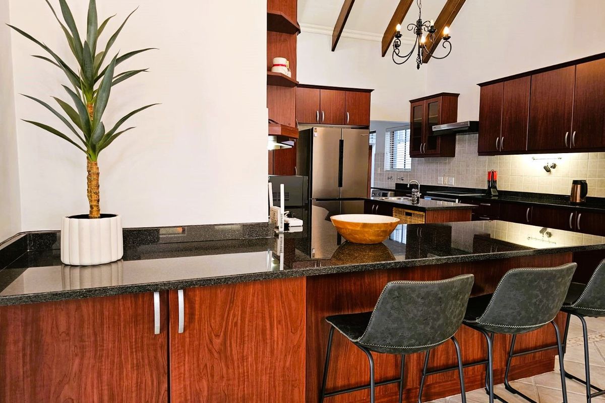 Spacious kitchen featuring dark wood cabinetry, granite countertops, a breakfast bar, and vaulted ceilings with exposed timber beams.