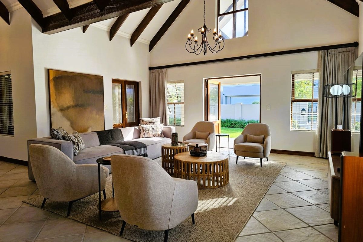 Spacious living room featuring high vaulted ceilings with exposed timber beams, tiled flooring, and large windows providing natural light and access to the garden.