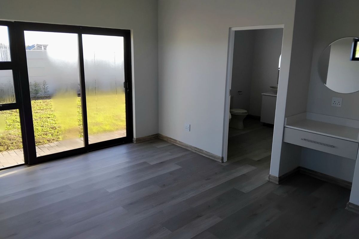 A bright bedroom featuring modern wood-look flooring, a built-in vanity area, and sliding glass doors providing direct access to the rear garden.