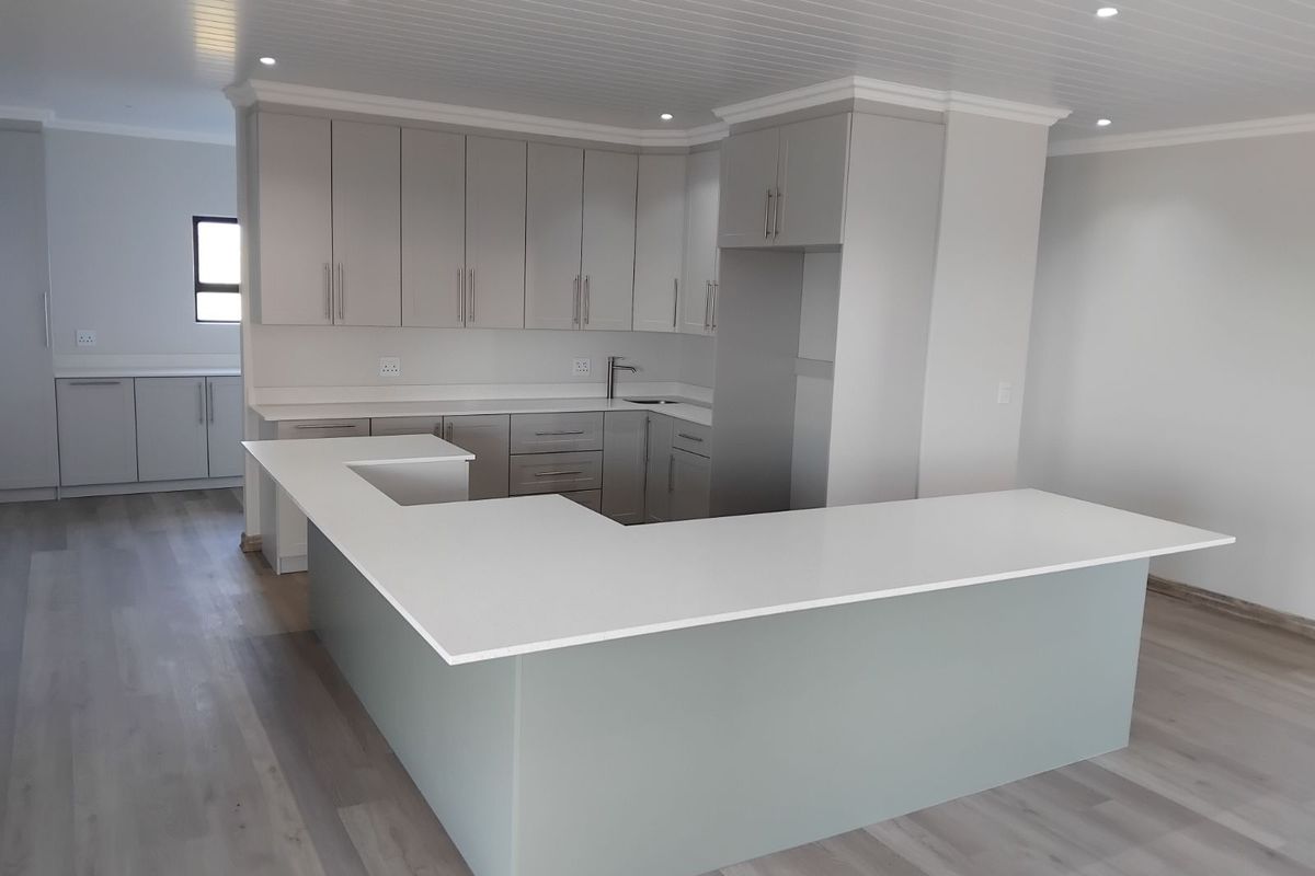 Modern kitchen featuring a large U-shaped island with stone countertops, ample cabinetry, and integrated storage, finished with light wood-look flooring and recessed lighting.