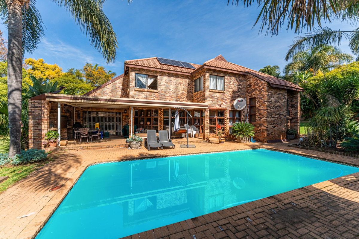 Rear view of a double-story brick house featuring a swimming pool, paved patio area, and solar panels on the roof.