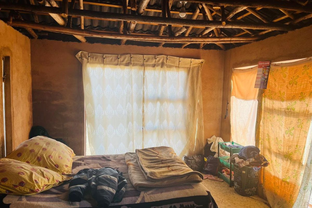 A rustic bedroom featuring exposed timber roof beams, natural wall finishes, and large windows allowing for natural light.