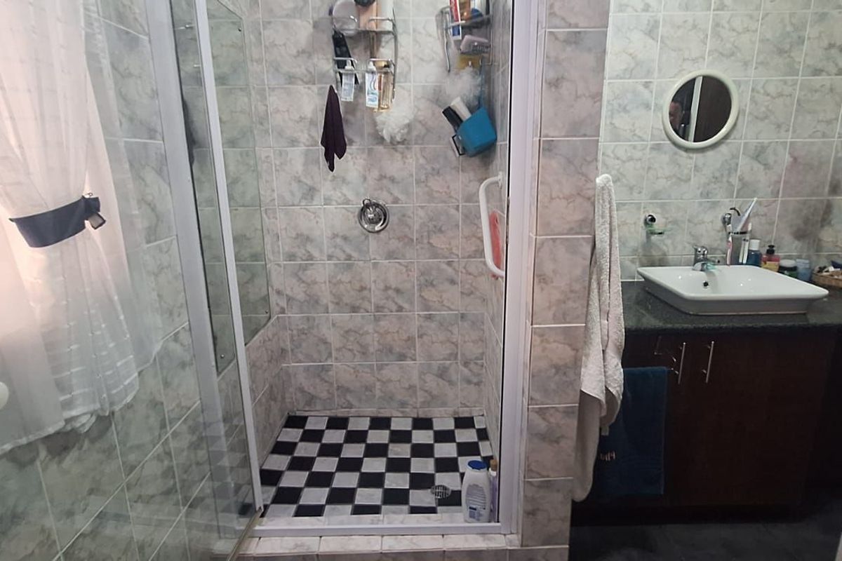 A functional bathroom featuring a glass-enclosed shower with a checkered floor, a vanity with a basin, and wall-mounted grab rails.