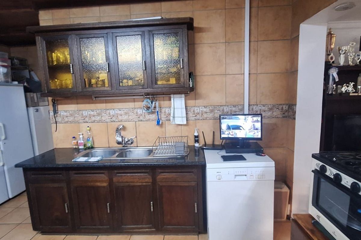 A dated kitchen featuring dark wood cabinetry, tiled walls, a double basin sink, and a built-in gas stove with an oven.