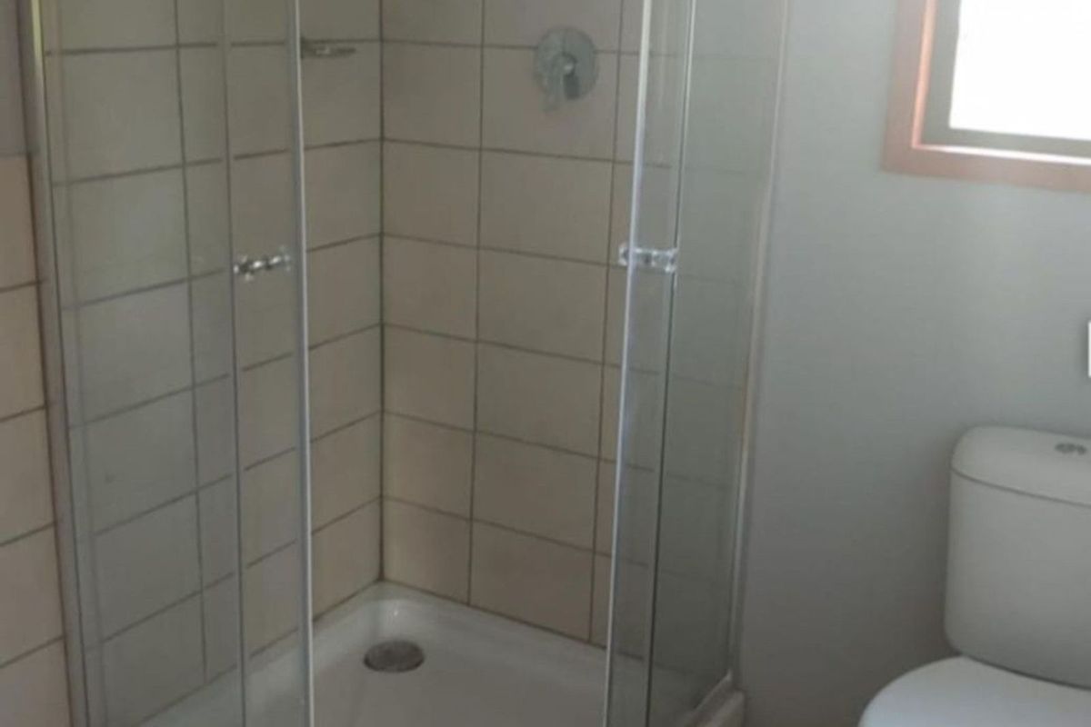 A functional bathroom featuring a glass-enclosed shower cubicle with tiled walls and a standard white toilet.