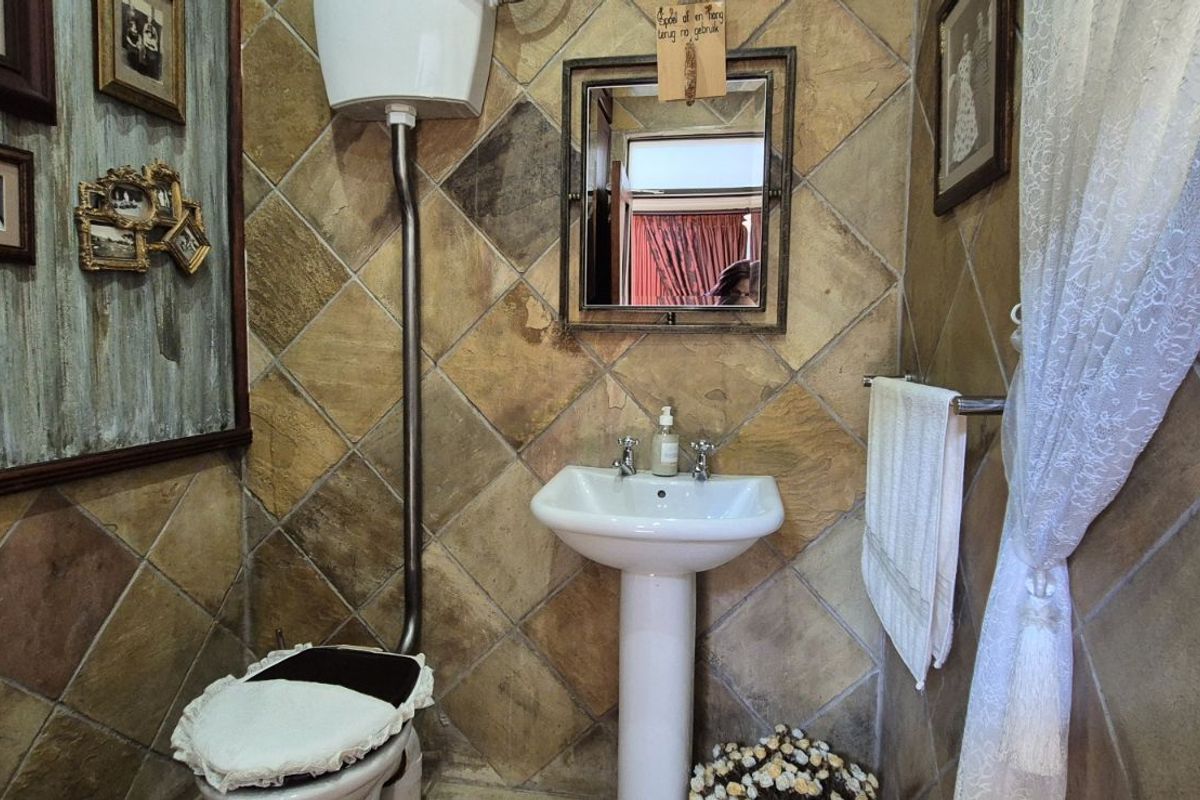 A compact bathroom featuring a pedestal sink and a high-level flush toilet, finished with rustic diamond-patterned wall tiles.