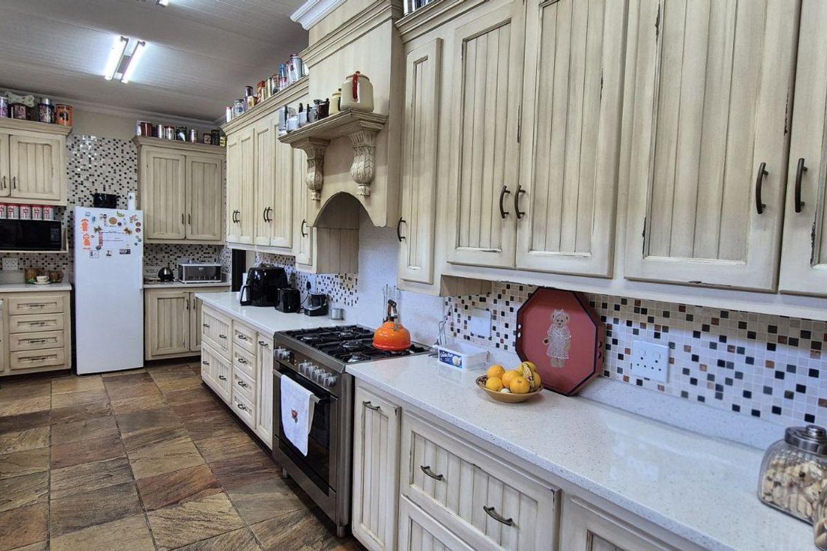 A spacious farmhouse kitchen featuring light-toned cabinetry, stone-look floor tiles, a gas range, and a mosaic tile backsplash.