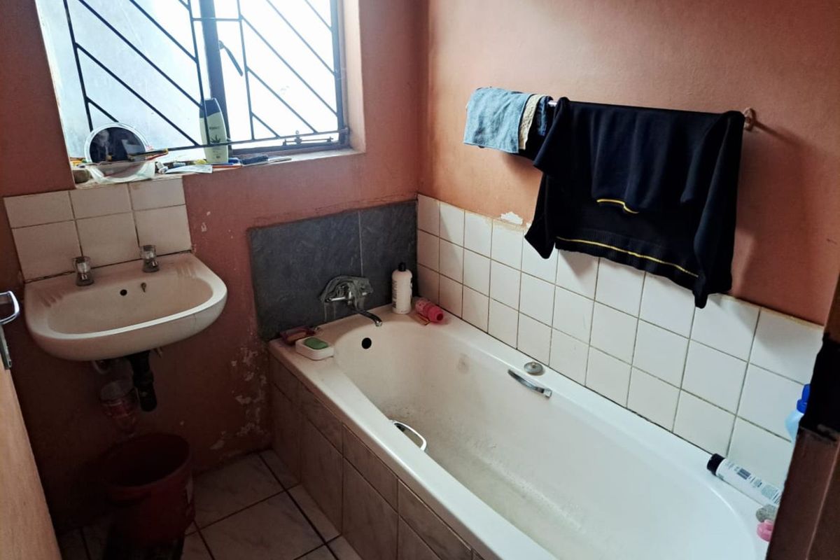 A compact bathroom featuring a standard bathtub, wall-mounted basin, and security bars on the window, requiring cosmetic updates to the wall finishes.