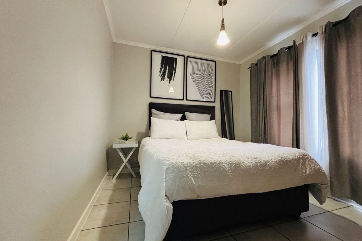 A well-maintained bedroom featuring neutral tiled flooring, a modern pendant light fixture, and large window with curtain tracks.