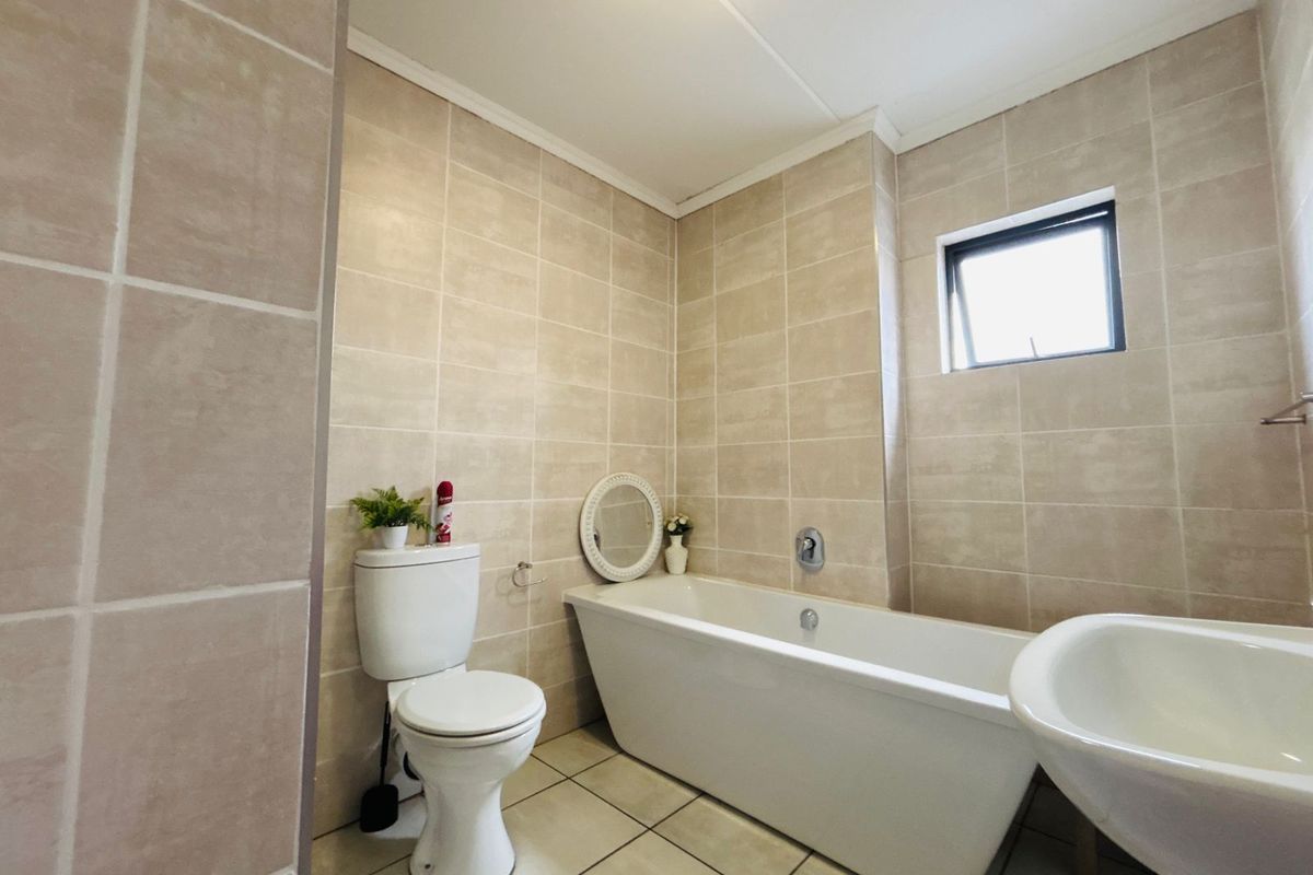 A functional bathroom featuring neutral wall and floor tiling, a built-in bathtub, and a standard toilet.