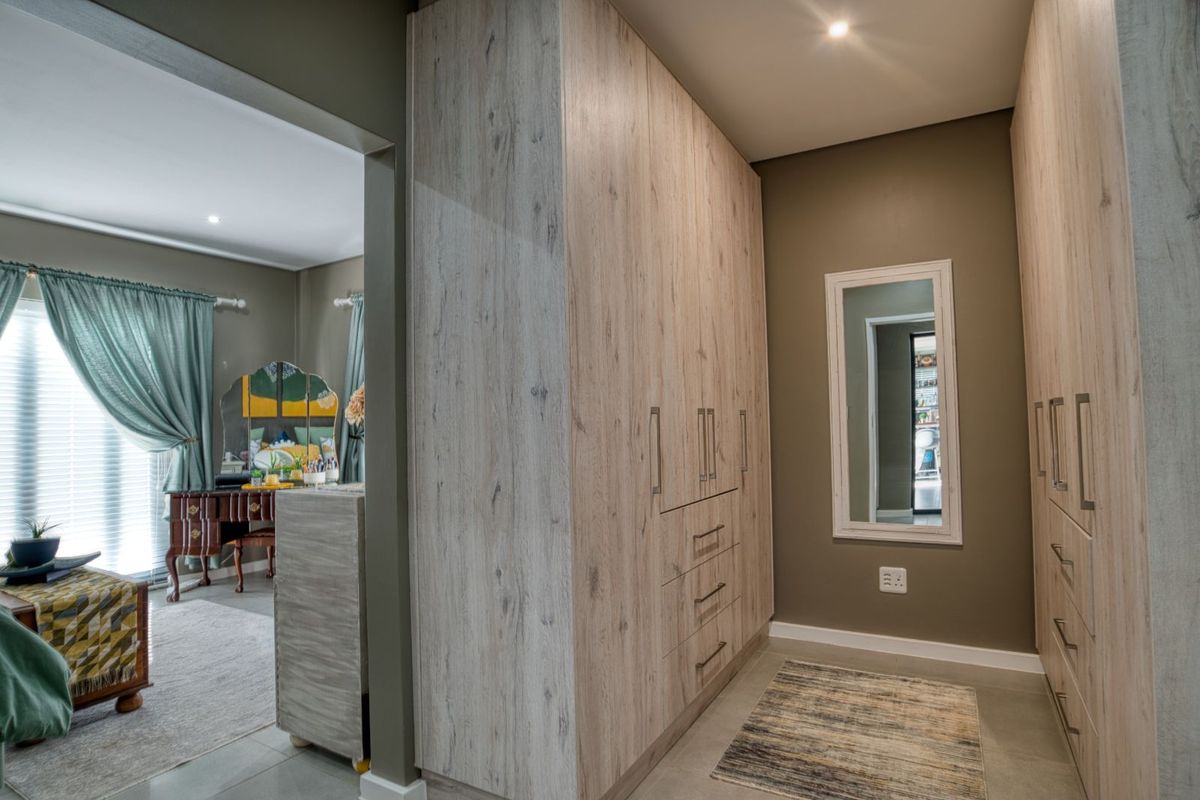 A walk-in dressing area featuring extensive built-in light wood-grain cabinetry with integrated drawers and shelving, adjacent to a bedroom space.