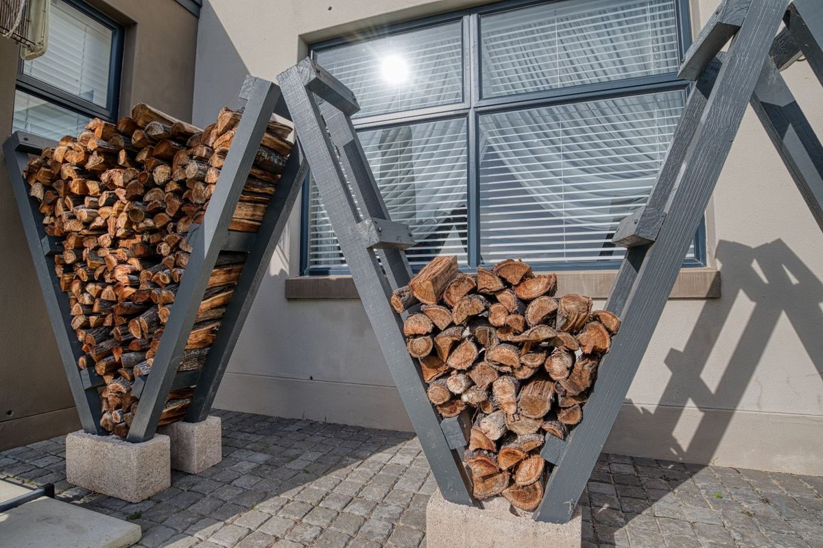 Exterior view of a paved area featuring custom V-shaped timber firewood storage racks against the building facade.