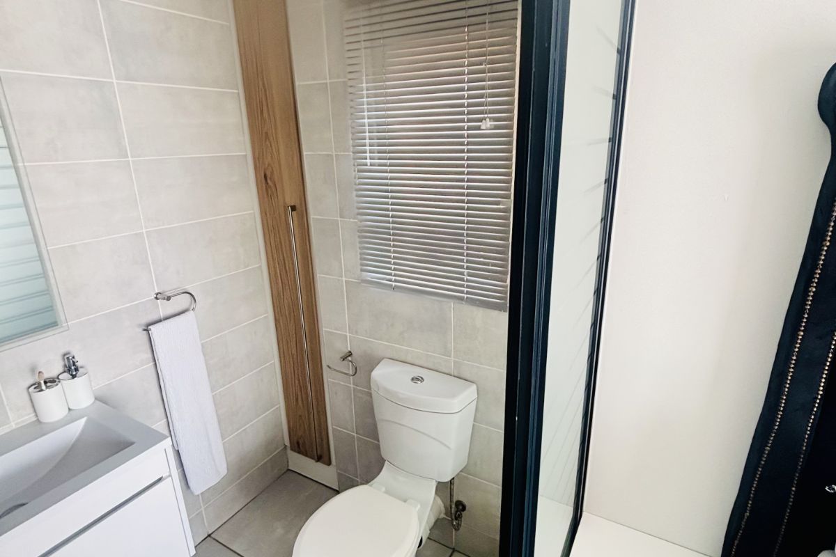 Modern bathroom featuring a wall-mounted vanity, ceramic toilet, and a glass-enclosed shower area with neutral floor-to-ceiling tiling.