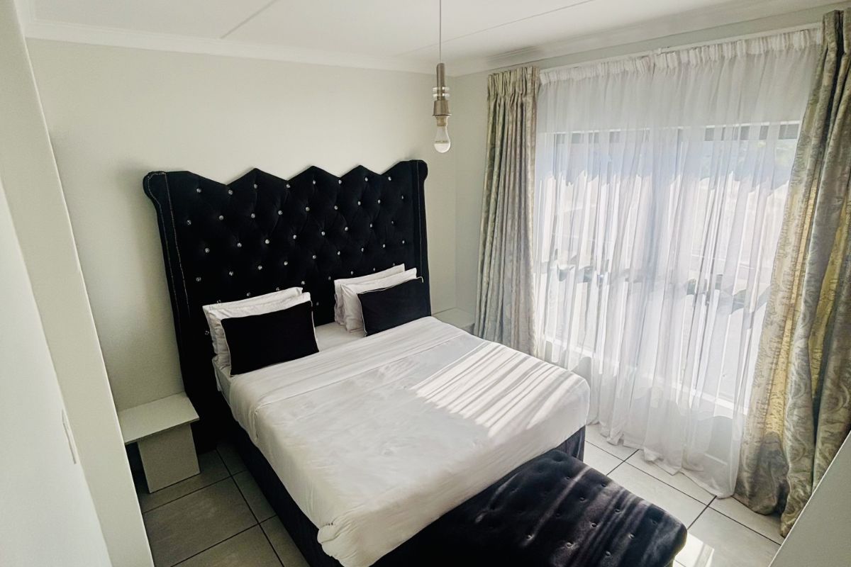 A well-lit bedroom featuring tiled flooring, neutral walls, and a large window with curtains, providing a comfortable and functional living space.