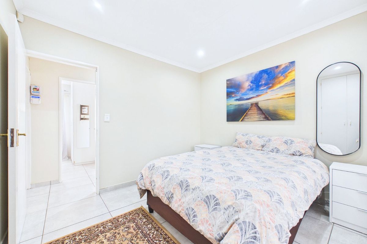 A well-maintained bedroom featuring neutral tiled flooring, recessed ceiling lighting, and a doorway leading to an adjacent room.