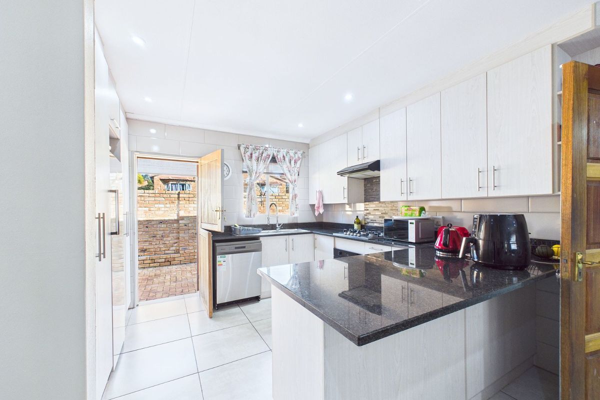 A functional kitchen featuring granite countertops, light-toned cabinetry, tiled flooring, and direct access to an outdoor paved area.