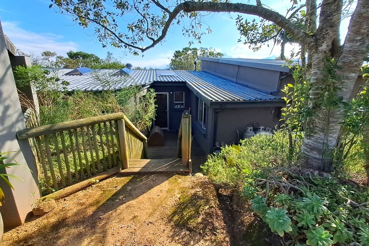 Exterior view of the farm property featuring a timber staircase leading to a modern dwelling with corrugated metal roofing and landscaped surroundings.