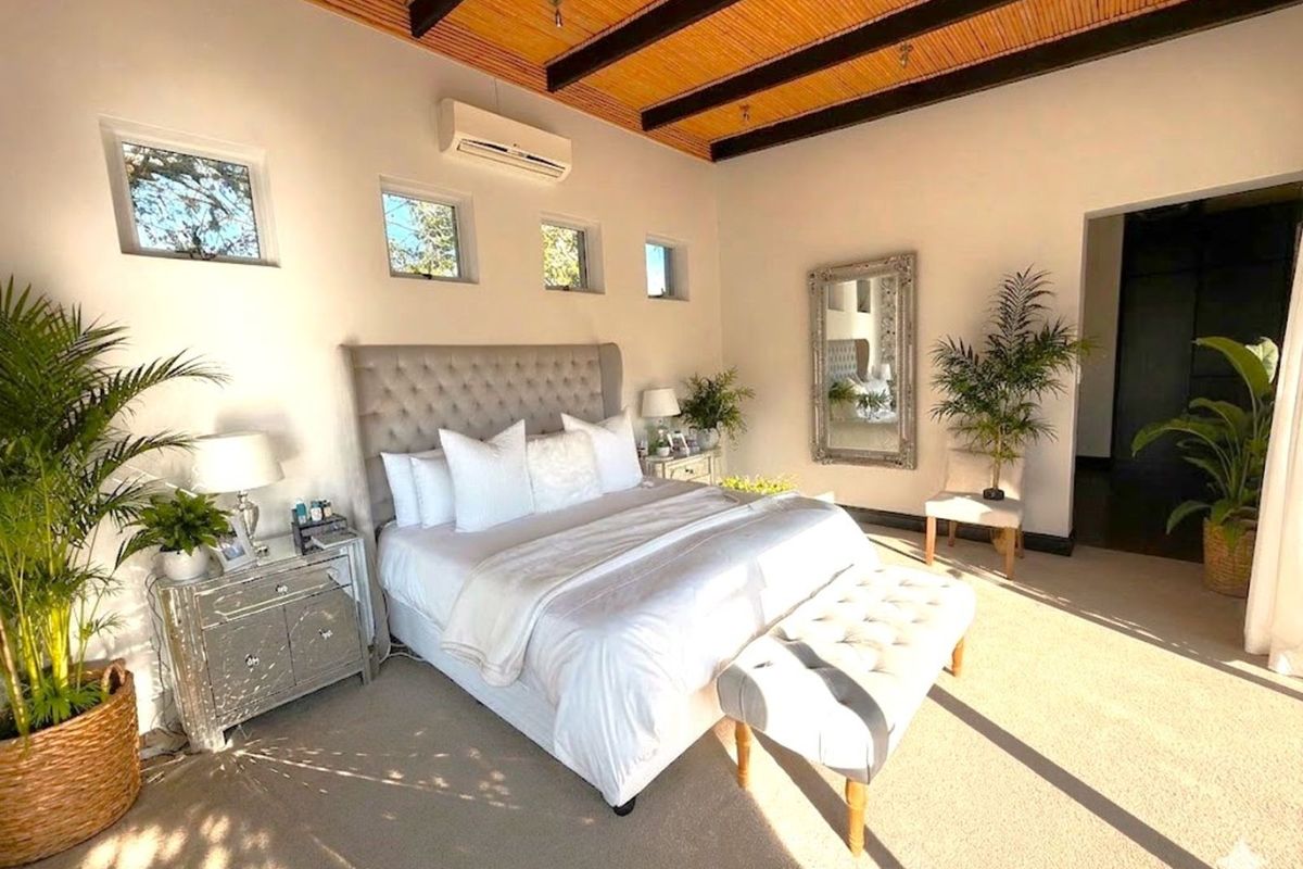 Spacious bedroom featuring high vaulted ceilings with exposed timber beams, wall-mounted air conditioning unit, and multiple windows providing natural light.