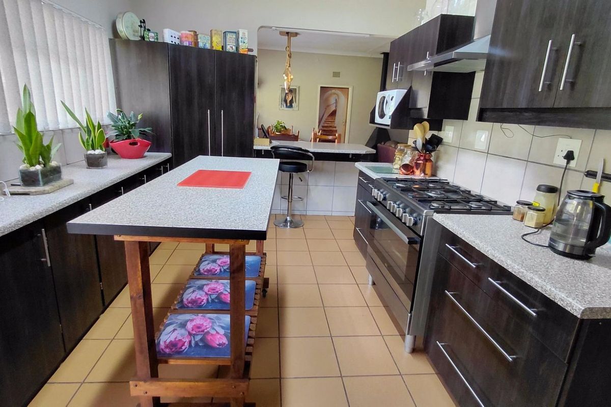 A functional kitchen featuring dark cabinetry, granite-style countertops, a gas stove with extractor fan, and tiled flooring.
