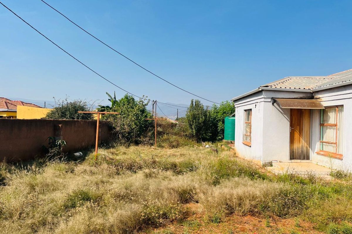A view of the rear exterior of the house featuring a large, unmaintained garden area, perimeter wall, and a simple rear entrance.