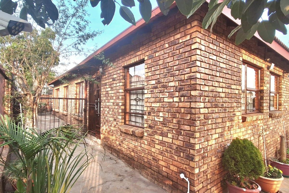 Exterior view of a face-brick house featuring security gates, metal window frames, and a paved walkway along the side of the building.
