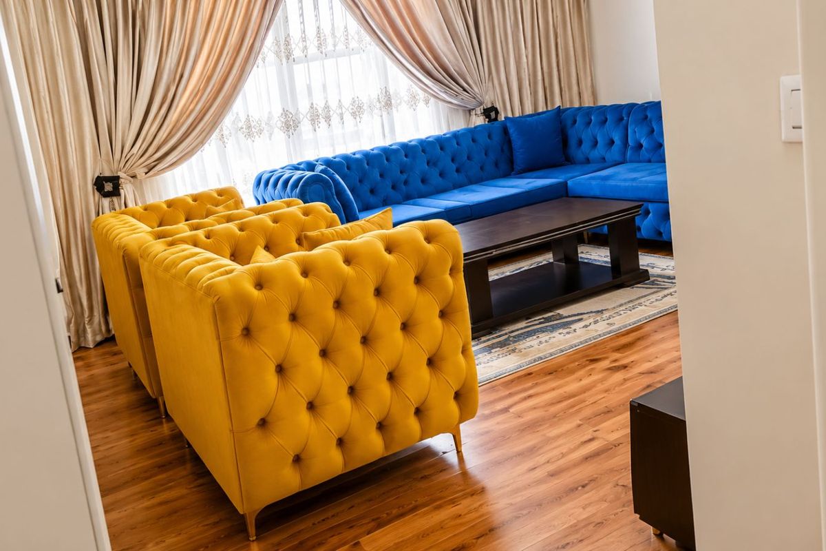 A well-maintained living room featuring warm-toned wood laminate flooring and large windows dressed with elegant floor-to-ceiling curtains.
