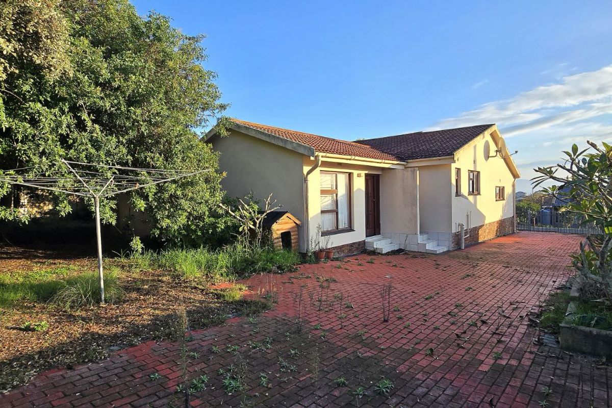 Rear view of the property featuring a paved courtyard area, established trees, and a tiled roof structure.