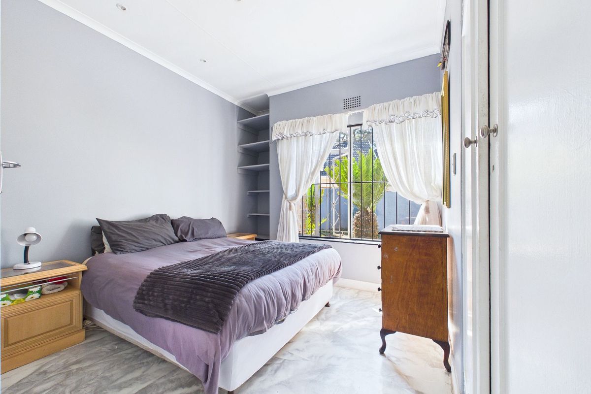 A bright bedroom featuring marble-look flooring, built-in shelving, and a window with security bars overlooking the garden.