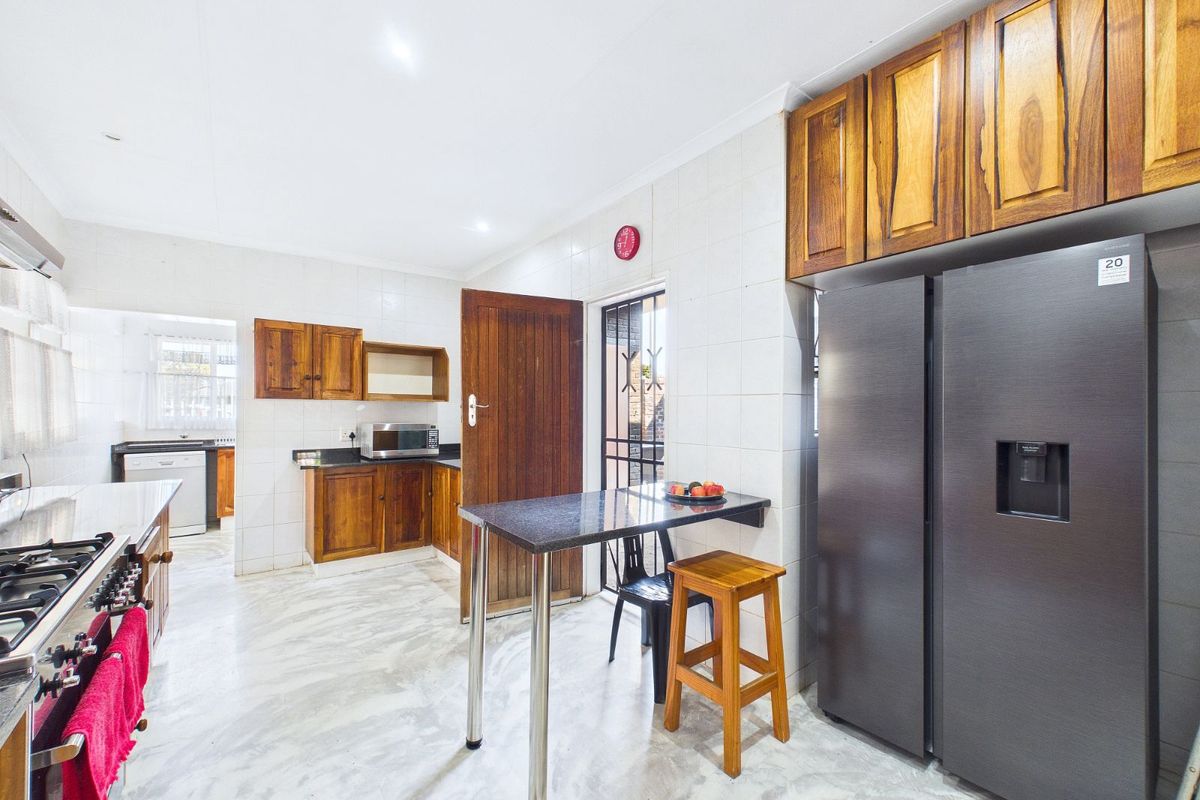 A functional kitchen featuring wooden cabinetry, granite countertops, a built-in gas hob, and tiled flooring, with an adjacent scullery area.
