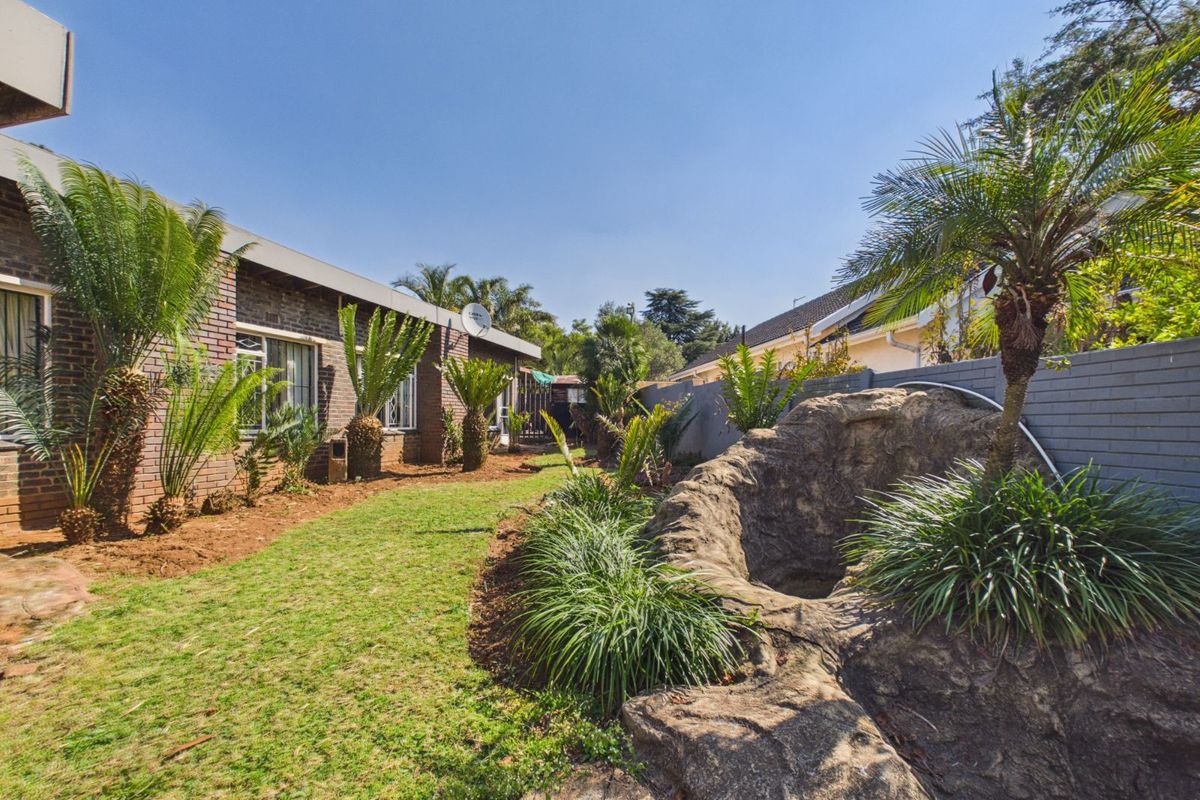 A rear garden area featuring a brick-faced house exterior, a lawn, and a decorative rock feature with integrated landscaping.