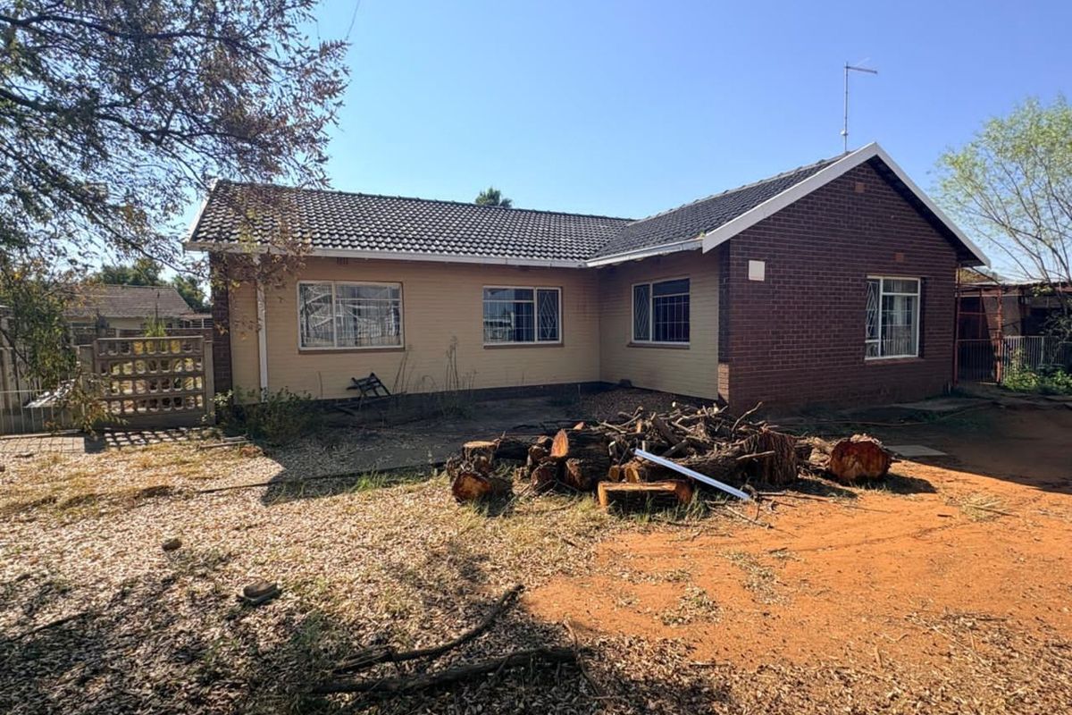 Rear view of a single-story brick and plaster house featuring a tiled roof, security bars on windows, and a large, unmaintained garden area.