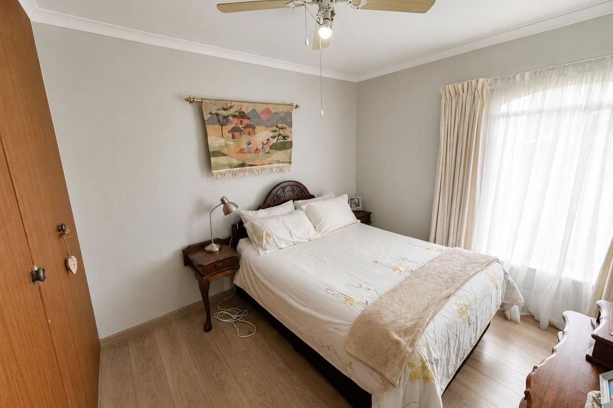 A well-maintained bedroom featuring light wood-look flooring, a ceiling fan, and built-in wooden cabinetry, offering a neutral and functional living space.