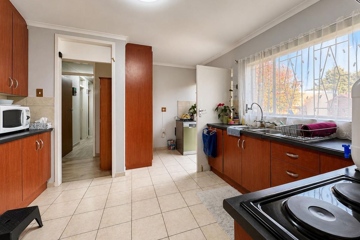 Functional kitchen featuring wood-look cabinetry, dark countertops, double basin sink, and tiled flooring with direct access to the hallway.
