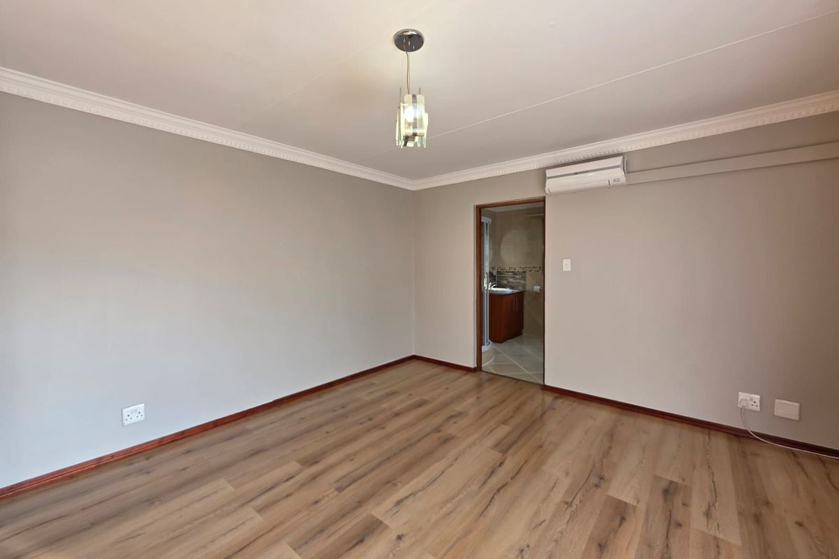 A spacious bedroom featuring wood-look laminate flooring, crown molding, a wall-mounted air conditioning unit, and an en-suite bathroom entrance.