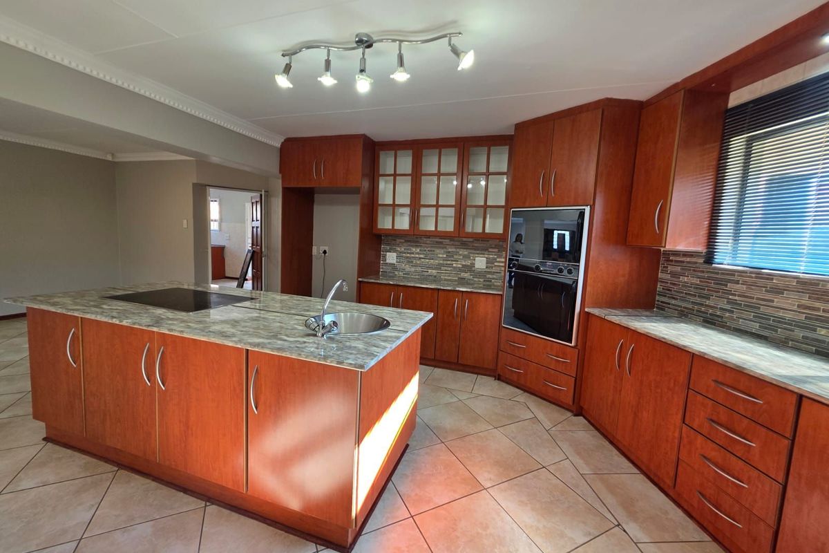 Spacious kitchen featuring wooden cabinetry, a central island with a built-in hob and sink, and integrated oven, finished with tiled flooring.
